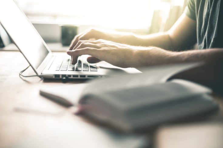 Person arbeitet an Laptop und ein Buch liegt im Vordergrund