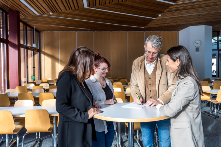 Vier Personen stehen um einen Tisch und diskutieren
