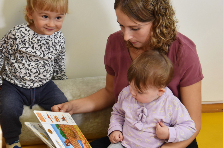 Fachperson betrachtet Bilderbuch mit zwei kleinen Kindern