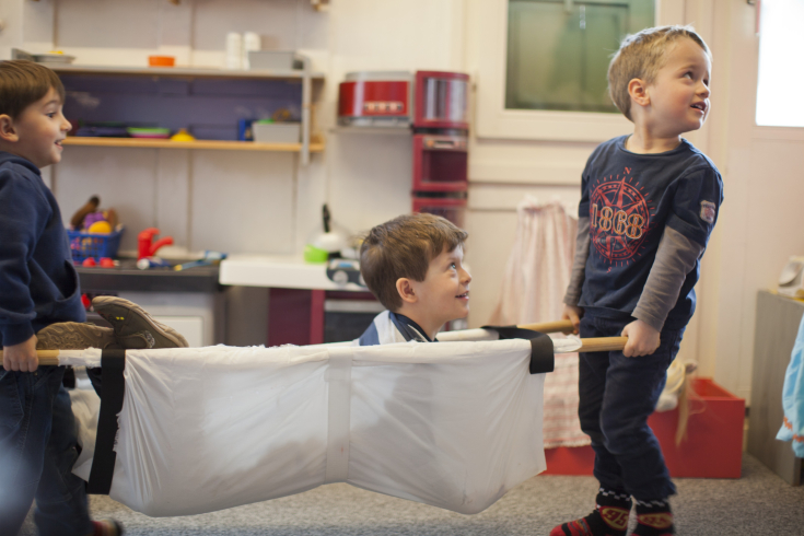 Zwei Kinder tragen ein Kind in einer Trage