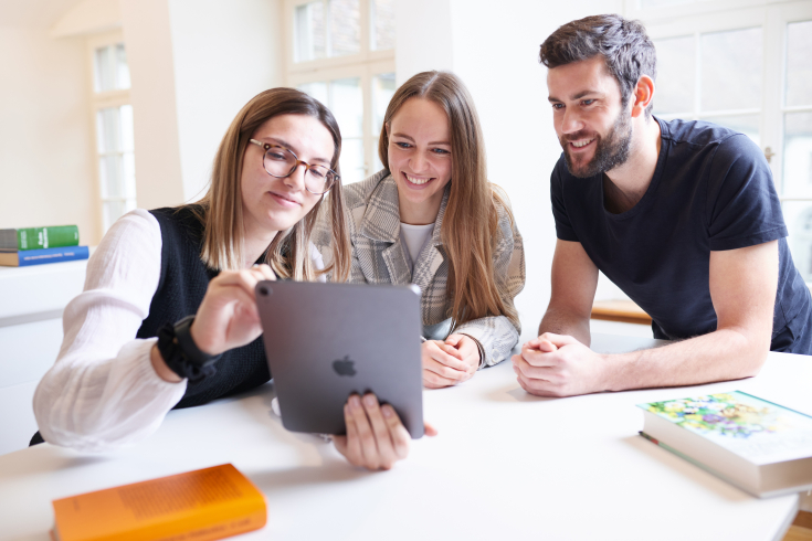 Drei Student:innen schauen auf ein Tablet