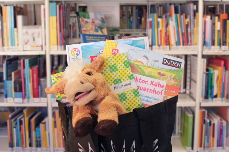 Schwarze Tasche ist mit Bauernhof-Medien befüllt und steht vor einem Bücherregal