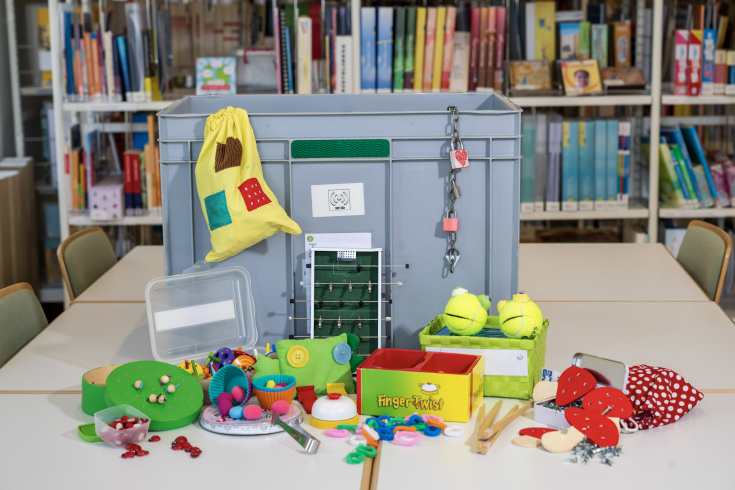 Graue Box mit vielen Spielsachen davor. 